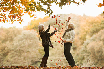 Older couple playing in autumn leaves - obrazy, fototapety, plakaty