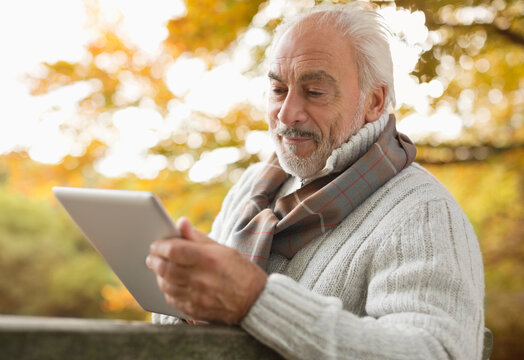 Older Man Using Tablet Computer In Park