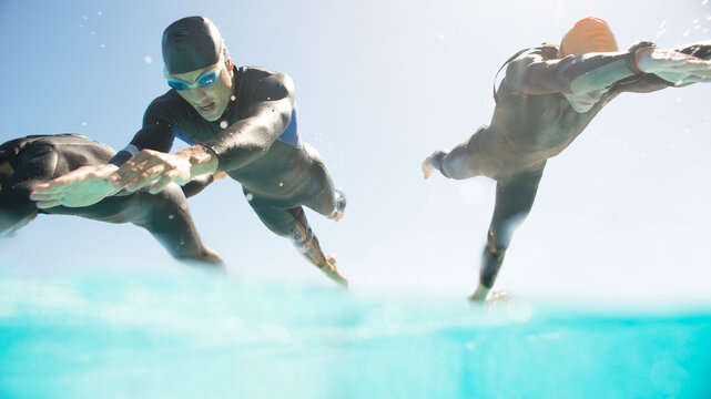 Triathletes in wetsuits running into ocean