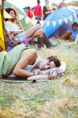 Man in sleeping bag sleeping outside tents at music festival