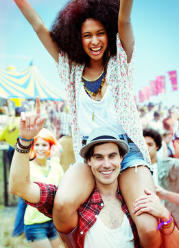 Portrait man carrying enthusiastic woman on shoulders at music festival