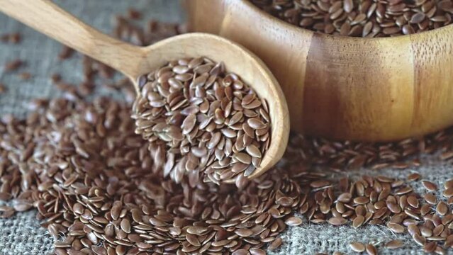 raw flax seeds in a wooden spoon and a wooden bowl on burlap (linen cloth)