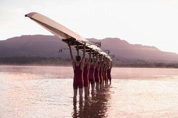Rowing team carrying row boat overhead in still lake - obrazy, fototapety, plakaty