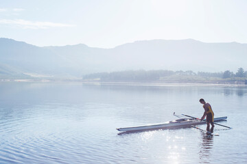 Naklejka premium Man placing rowing scull in lake