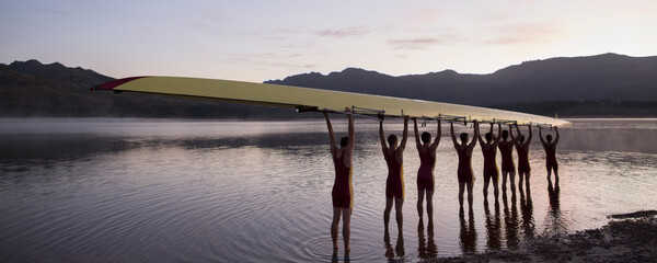 Rowing crew holding scull overhead in lake
