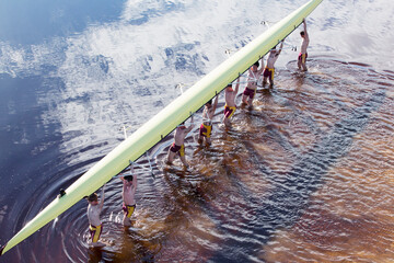 Rowing crew carrying scull overhead in lake