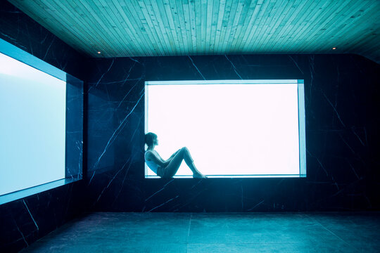 Woman sitting on ledge at window in pool room