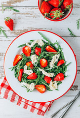 Fresh summer strawberry salad with arugula and stracciatella on white plate over rustic wooden background