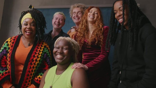 Handheld shot of six LGBTQIA queer people smiling and laughing against studio backdrop