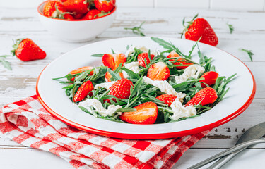 Fresh summer strawberry salad with arugula and stracciatella on white plate over rustic wooden background