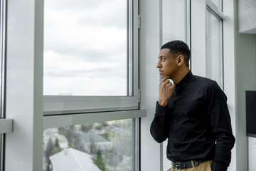 Fototapeta premium Thoughtful young man standing near the window