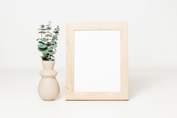 Wooden mockup photo frame with ceramic vase and eucalyptus leaves on white wooden table. Minimal...