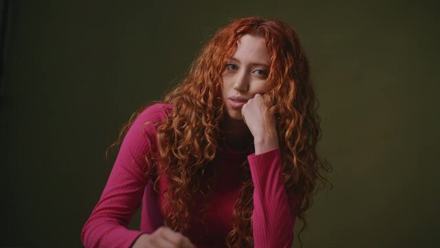 Lesbian woman with long red curly hair against studio backdrop