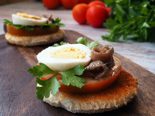 Toasts with tomato, egg and anchovy on a wooden board