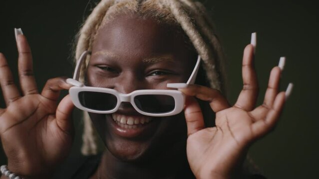 Cheerful black lesbian woman holding sunglasses in front of face