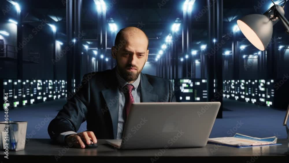 Poster businessman using laptop in server room, working on big data hardware service at desk. it specialist