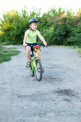 Fototapeta premium teenager boy in helmet and green T-shirt riding a bike on the gravil road in summer