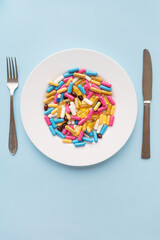 Tablets, capsules, vitamins and natural organic food supplements on a white plate on a blue background. Minimal modern pharmacy or healthcare concept. Vertical photo.