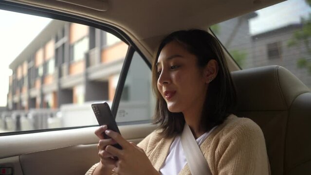 Relaxing moment of beautiful woman sitting in car back seats using smartphone play social media with safety belt and look out the window. Female happy in car traveling on the road to destination. - Powered by Adobe