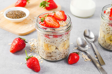 Overnight Oats with Fresh Strawberry, Banana and Chia Seeds in Jars on Light Grey Background,...