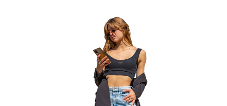 Young, tanned, beautiful woman in a black top, cold shoulder jacket and jeans with sunglasses and long blonde hair, looking, reading, typing on her mobile phone on a PNG background