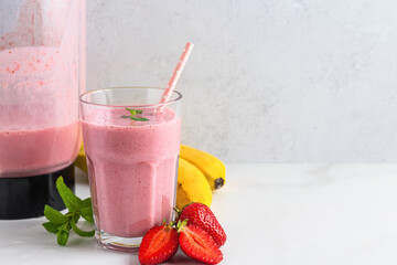 Glass of strawberry and banana smoothie with fresh juicy fruits and blender for making healthy...