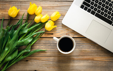 Laptop, a cup of coffee and a bouquet of tulips on a wooden background.