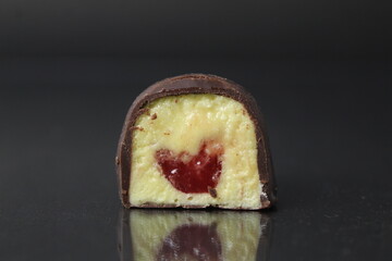 Chocolate body candy in a section, close-up on a black, gray, dark background with a yellow filling: fruits: maango, banana, papaya and red berry, raspberry, strawberry, cherry. Handmade candies