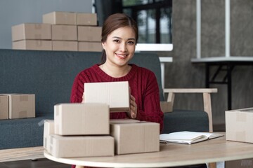 Happy young asian woman startup small business freelance holding parcel box and computer laptop and sitting sofa, Online marketing packing box delivery concept
