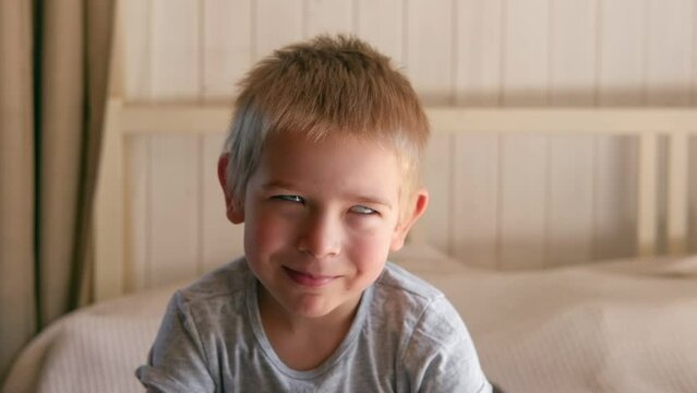 Boy joking, sticking tongue out with silly expression. Child making face. Funny foolishness portrait of little baby boy on the bedroom background. Adorable caucasian kid making crazy comical gesture