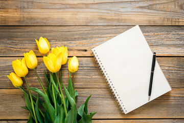 Naklejka na ściany i meble Blank notepad and yellow tulips on a wooden background, top view.