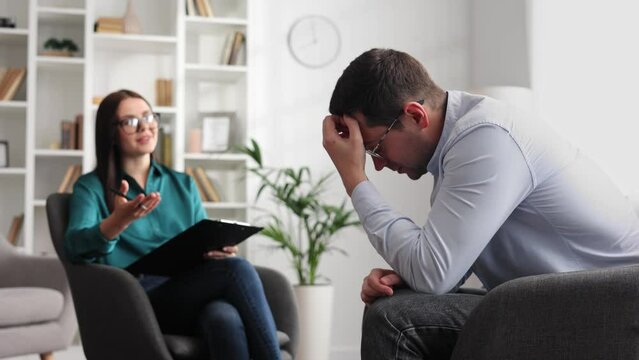 A professional psychologist consults a male patient in a state of stress and depression, who is sitting in a chair in the office. She writes on paper. The concept of a consultant psychologist.