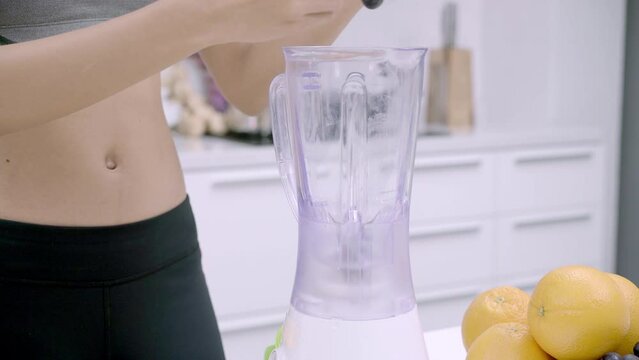 Woman in sportswear preparing an energizing fruit juice after exercise with a blender in the kitchen