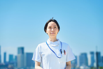 晴天の街並みの前に立つ白衣の女性