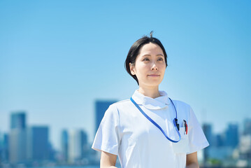 晴天の街並みの前に立つ白衣の女性