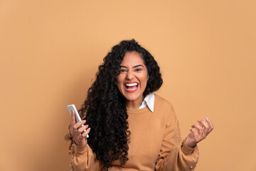 excited black young woman raising arms and celebrating in beige background. celebration, positive, success concept.