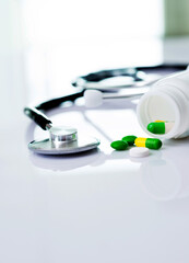 Stethoscope and some pills on white table