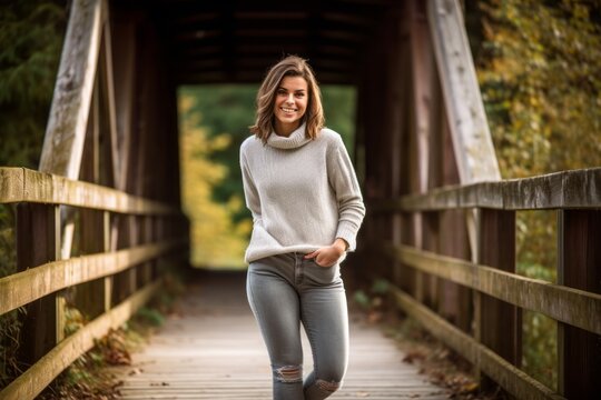 Conceptual portrait photography of a grinning girl in her 30s wearing a comfortable pair of jeggings against a rustic bridge background. With generative AI technology