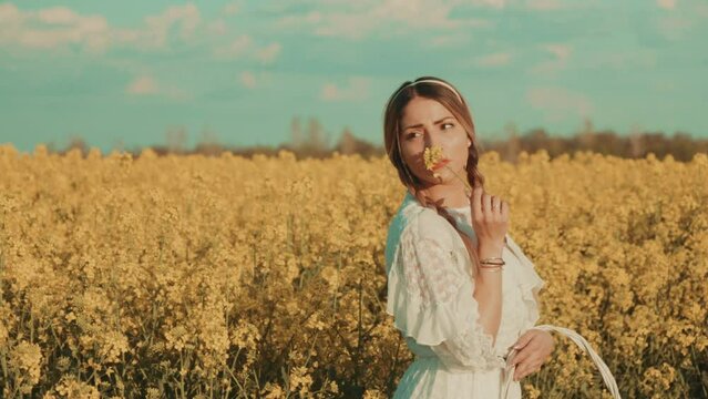 Beautiful young woman in white dress on yellow flower meadow in sunset