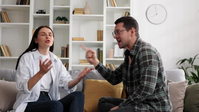 A young couple is sitting on the sofa in the living room, emotionally arguing about important things, discussing problems in the relationship, they cannot come to an agreement.