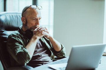 Middle-aged man fully focused on work he looks intently at computer on table. Deep in thought, he...