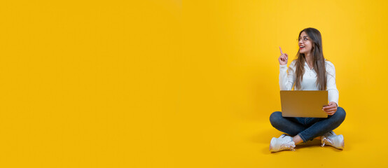 Perfect offer concept, cheerful caucasian girl sitting floor with laptop. Isolated yellow studio background. Young lady pointing finger copy space. Banner design idea. Browsing internet, recommending.