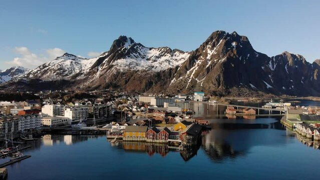 Aerial drone shot of a small town in Lofoten, Norway with a big mountain chain in the background.