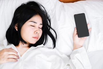 Nomophobia Concept with Asian Woman Sleeping with Hand Still Clutching Mobile Phone, Symbolizing the Constant Need for Phone Proximity