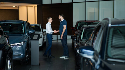 Seller and buyer shake hands in a car dealership. Caucasian man buys a car.