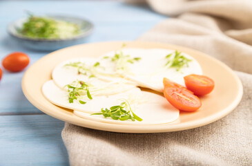 White cheese with tomatoes and cilantro microgreen on blue. side view, selective focus.