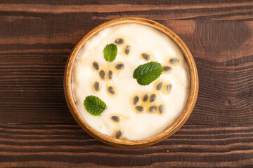 Yoghurt with granadilla and mint in wooden bowl on brown wooden, top view.