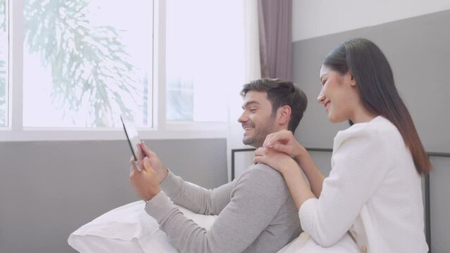Man and woman using tablet to take pictures in bed. Young man and woman Couple booking hotel booking via tablet.