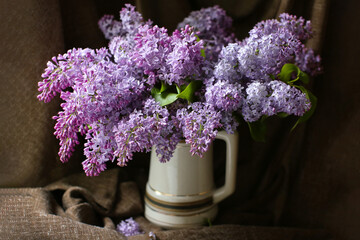 Bouquet of blooming lilac in a vase on a dark textile background