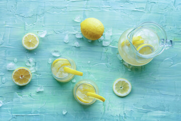 Lemonade. Lemon water drink with ice. Two glasses and a pitcher on a blue background, overhead flat...